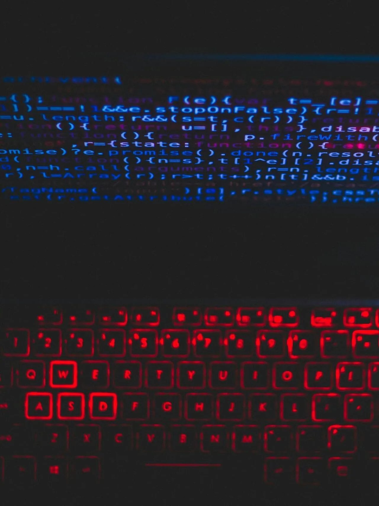 Dark-themed laptop setup with a red glowing keyboard and code on screen, ideal for tech enthusiasts.