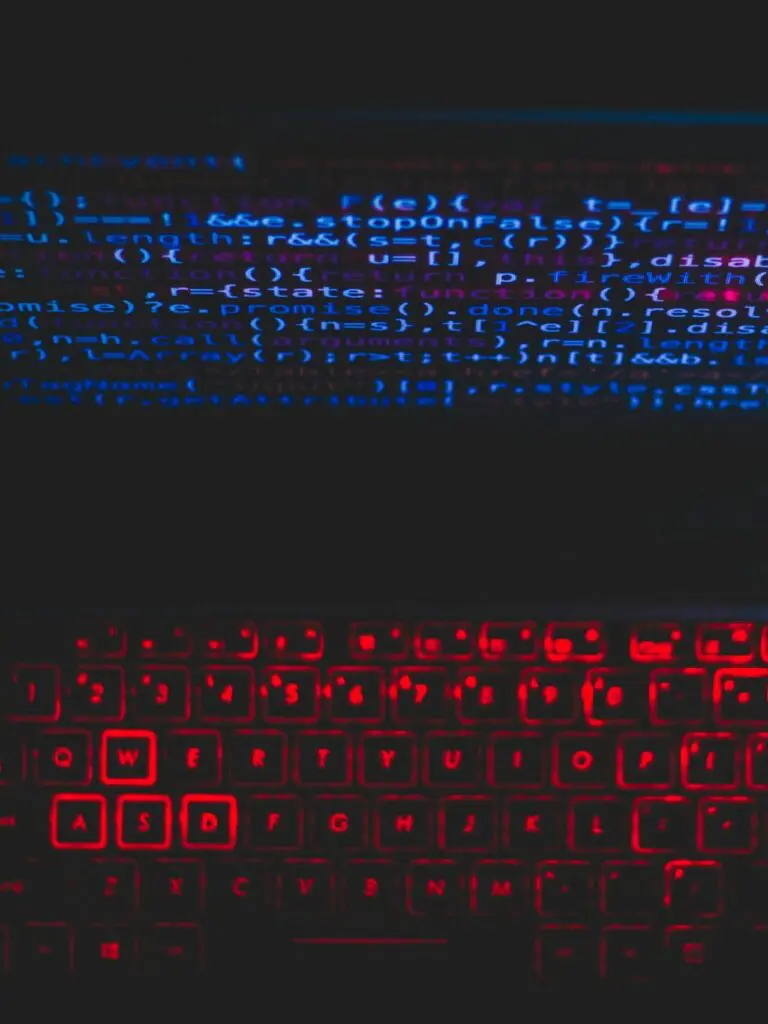 Dark-themed laptop setup with a red glowing keyboard and code on screen, ideal for tech enthusiasts.