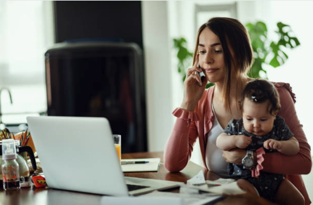 Woman holding baby and working on laptop