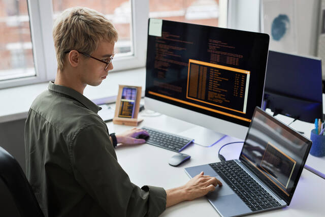 computer user at a desk with a laptop and external monitor