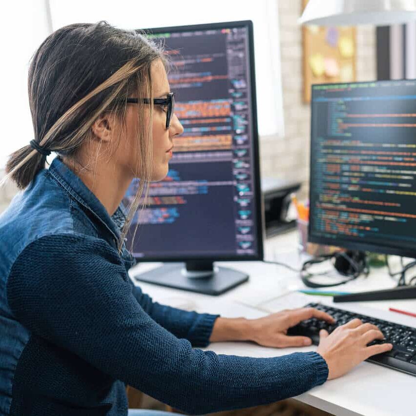 Female freelance developer coding and programming. Coding on two with screens with code language and application.