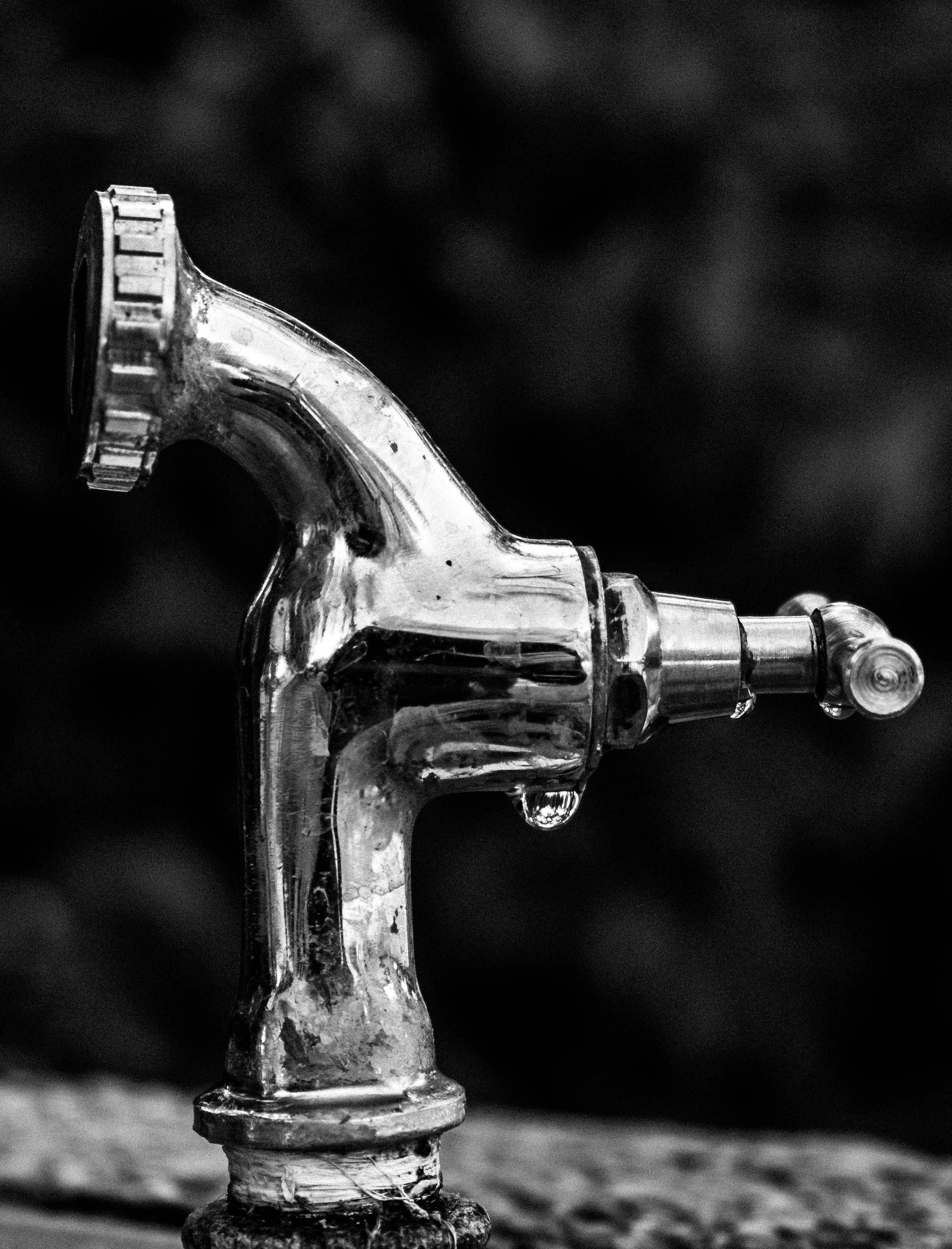 A detailed black and white image showcasing a chrome water faucet with water droplets.