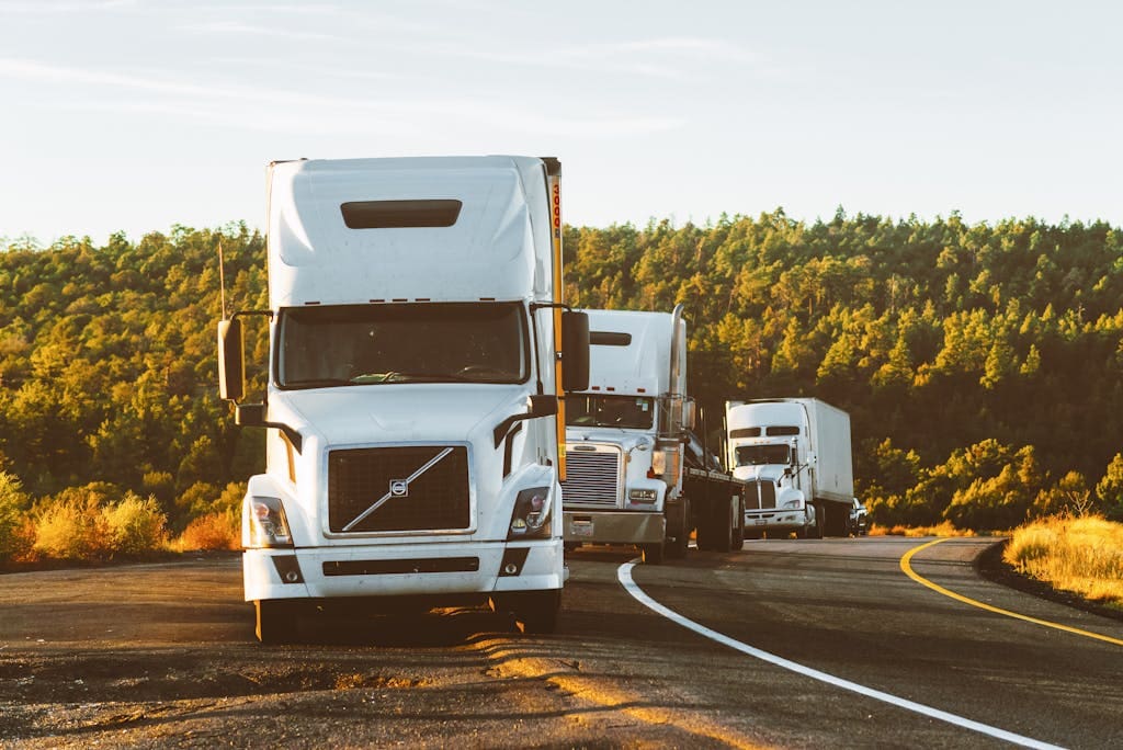 Three semi trucks driving on a highway through a forested landscape in Arizona.