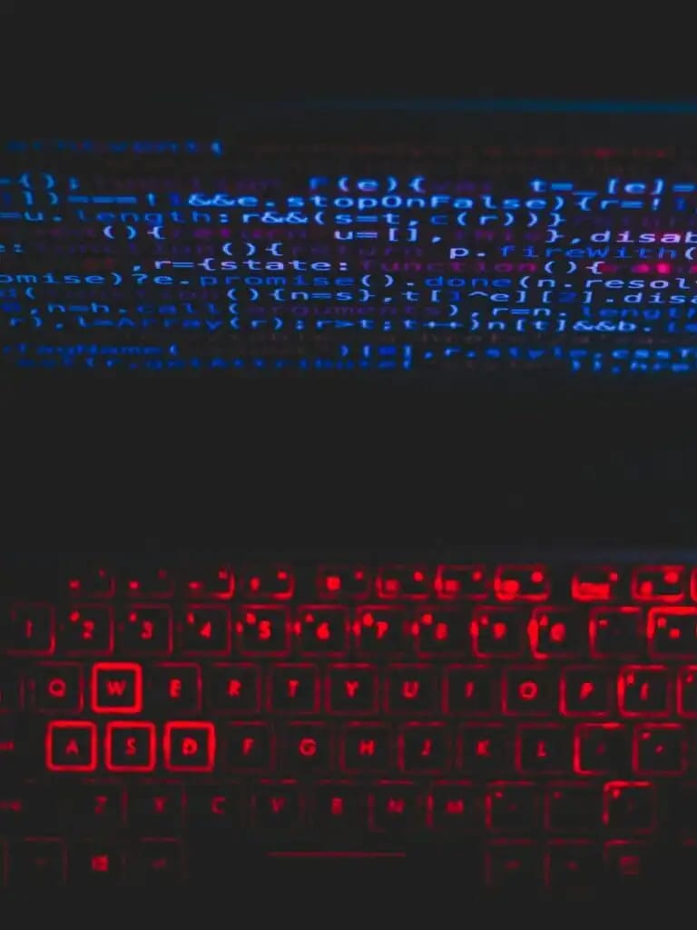 Dark-themed laptop setup with a red glowing keyboard and code on screen, ideal for tech enthusiasts.