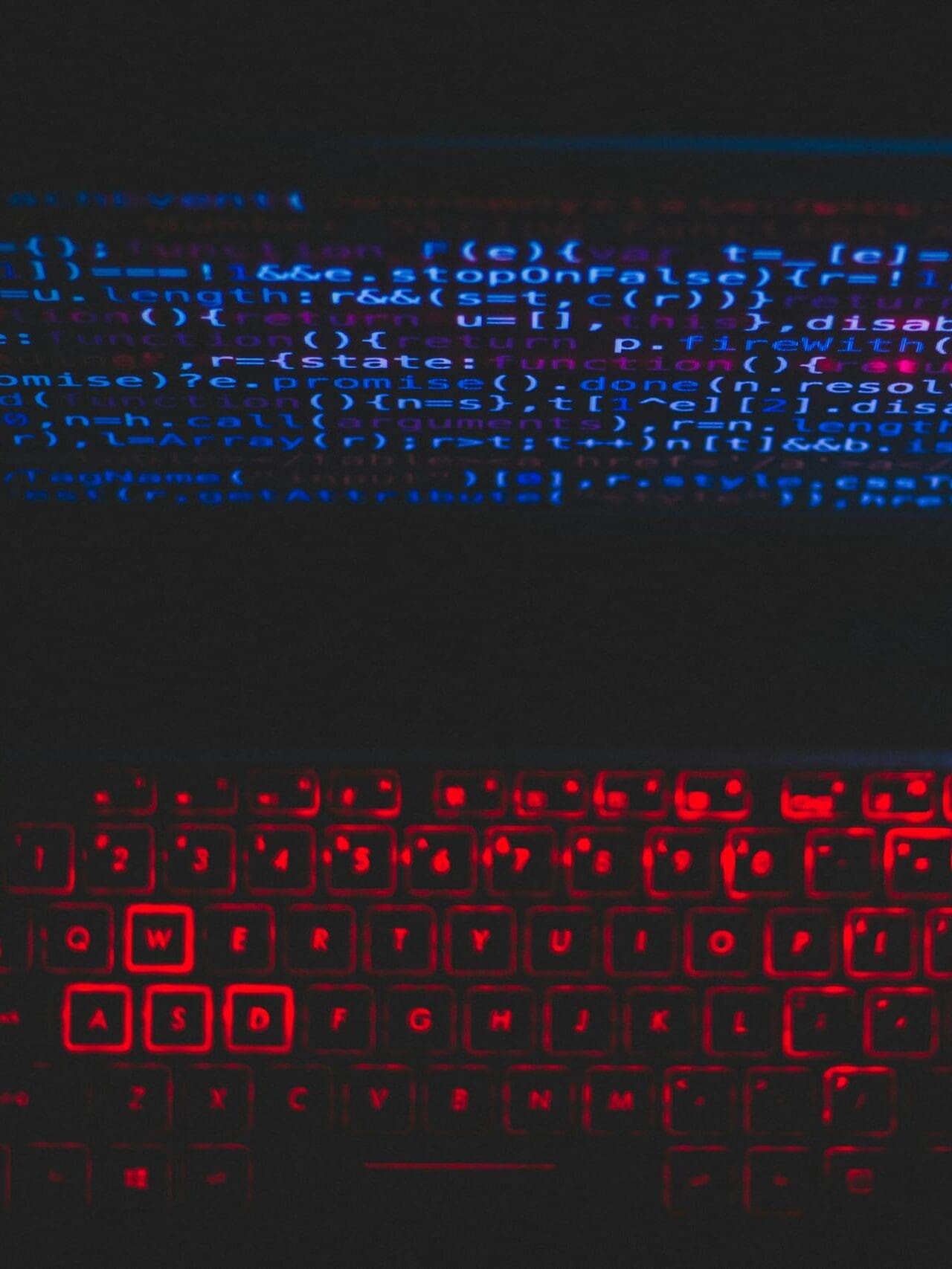 Dark-themed laptop setup with a red glowing keyboard and code on screen