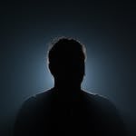 A silhouette of a mysterious figure illuminated by backlight, creating a dramatic and moody effect.
